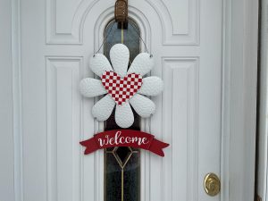 Lovely daisy with red/white checkerboard heart and “Welcome” banner in sturdy metal with hangers for your door. 18”by 12.” Free shipping.